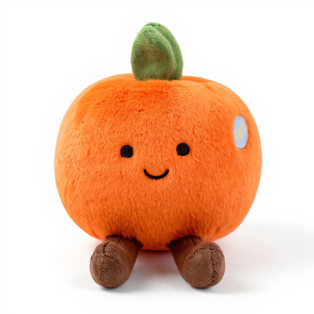 Peluche ronde en forme d’orange avec un petit sourire, des pattes marron et une feuille verte sur la tête, posée sur fond blanc.