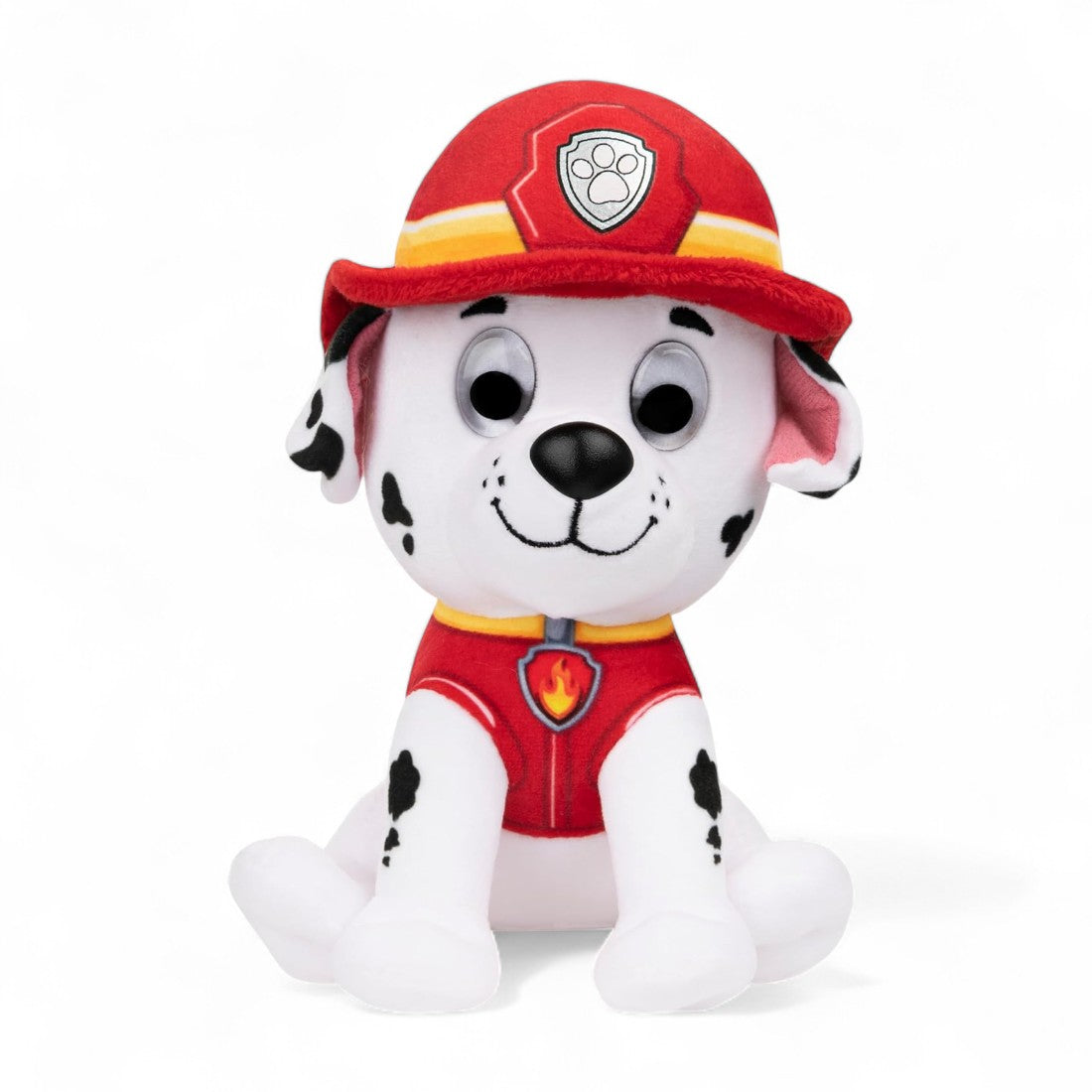 Peluche Marcus de la pat' patrouille, dalmatien blanc à taches noires, tenue rouge et casque de pompier rouge, assise et souriante sur fond blanc.