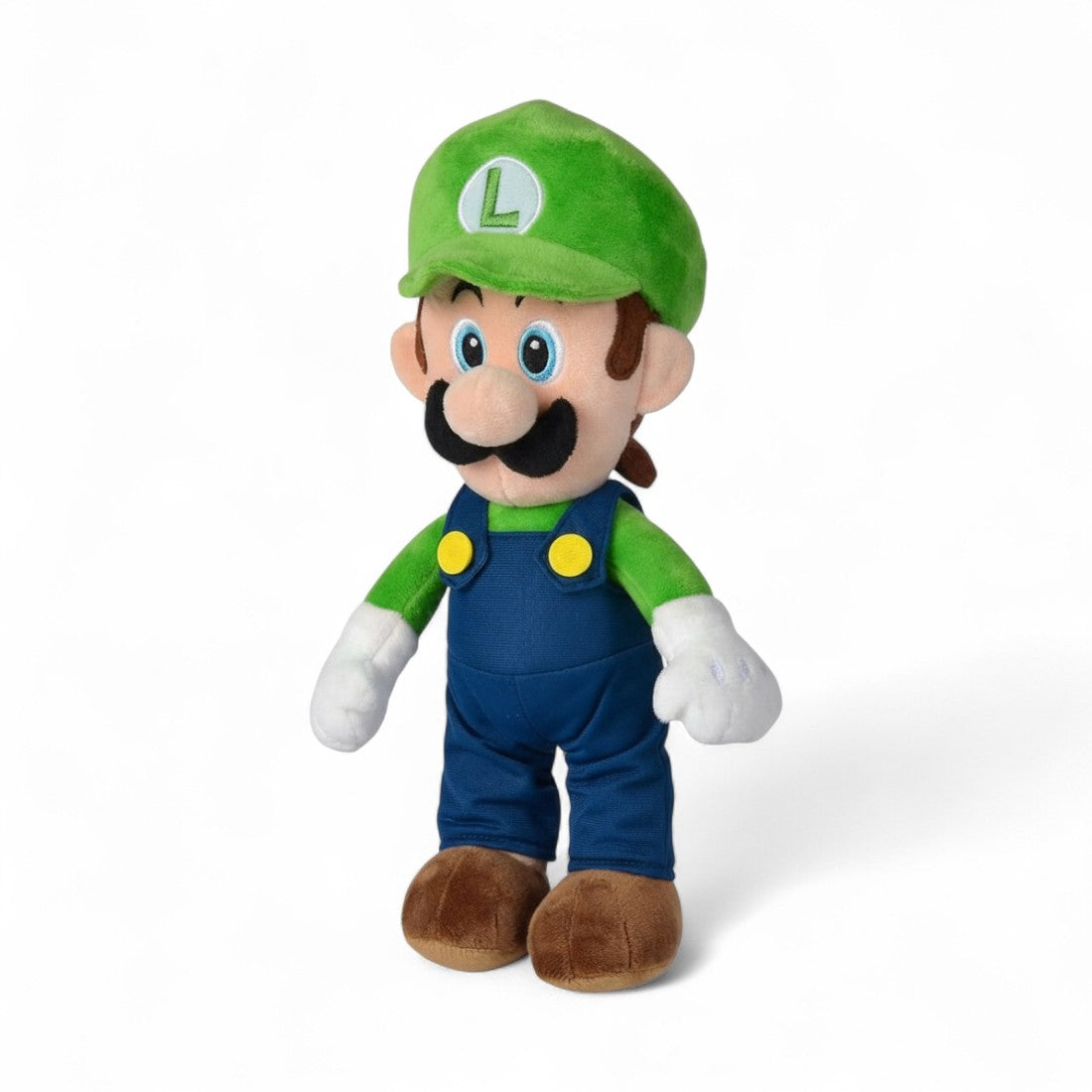 Peluche Luigi de Super Mario Bros, casquette verte avec “L”, salopette bleue, moustache noire, yeux bleus, en position debout sur fond blanc.