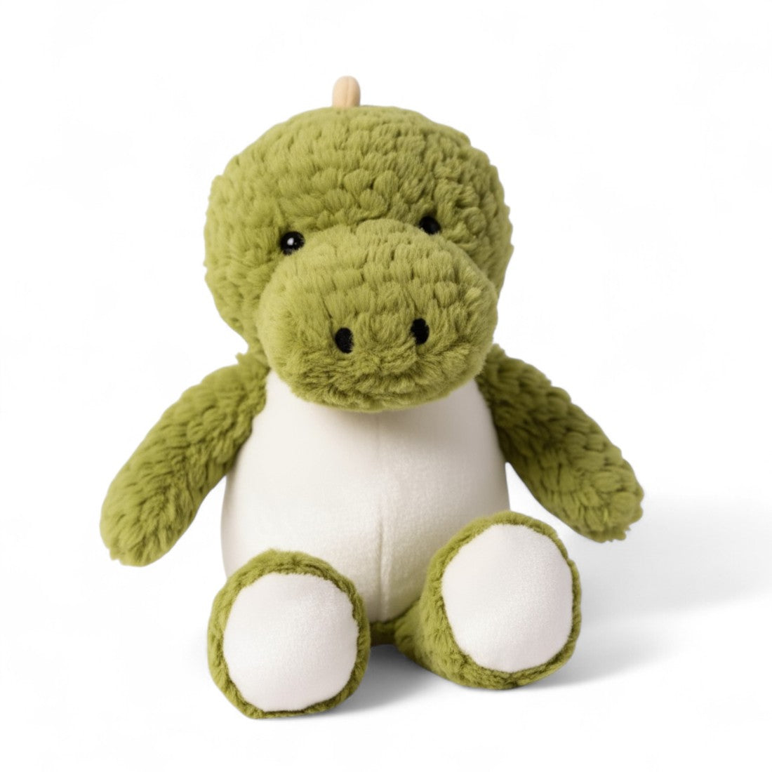 Peluche dinosaure vert, ventre blanc, museau large, yeux ronds brodés, crête jaune pâle sur la tête et le dos, forme assise moelleuse, sur fond blanc