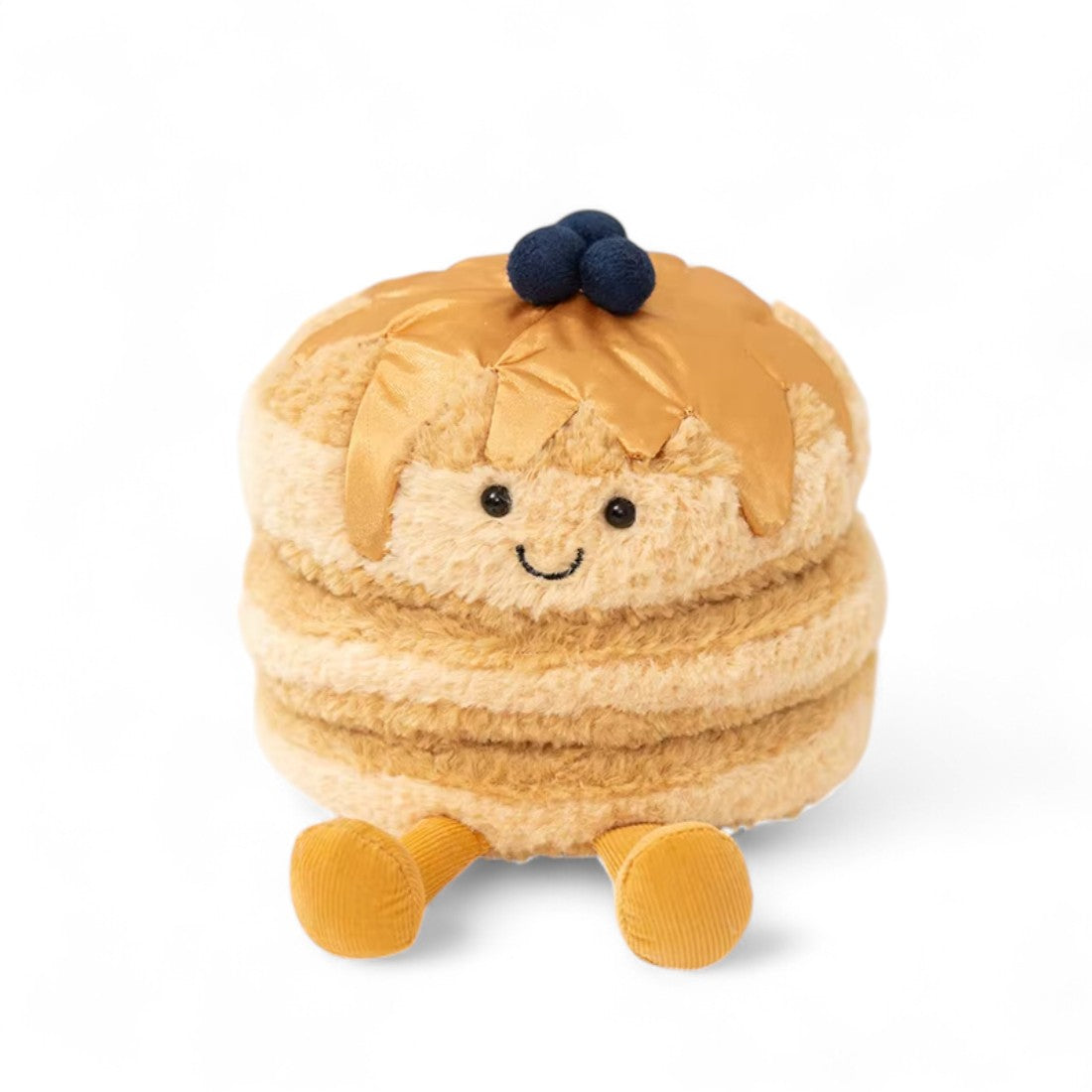 Peluche pancakes beige avec un visage souriant, jambes jaunes et petites myrtille bleues sur le dessus, assise sur fond blanc