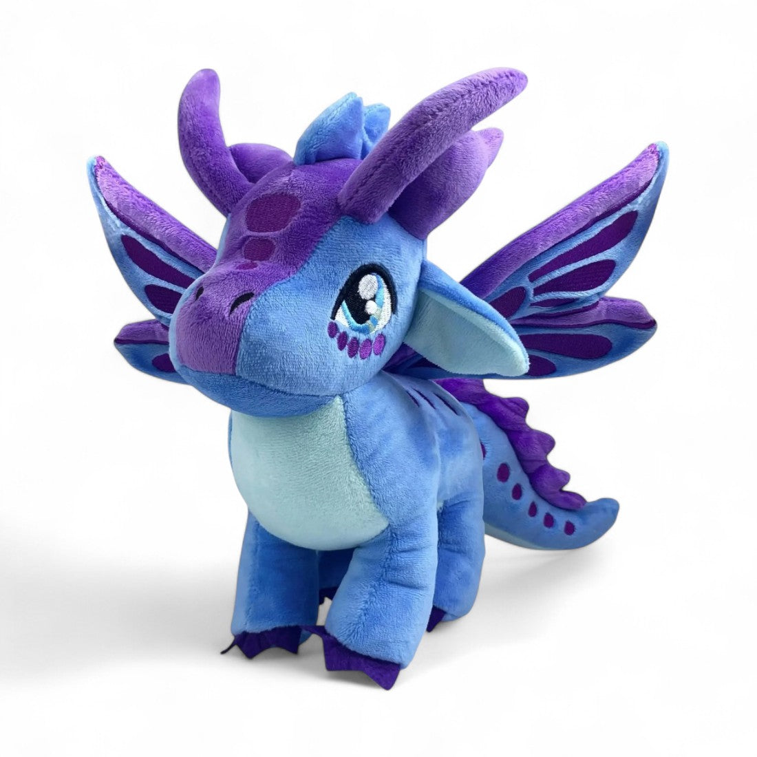 Peluche dragon bleu et violet aux ailes façon papillon violettes, cornes violettes, yeux clairs, sur fond blanc