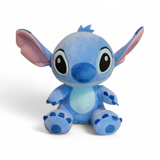 Peluche Stitch bleue de 25 cm assise, avec grandes oreilles et sourire tendre, sur fond blanc.