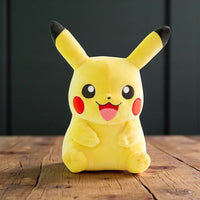 Peluche pokémon - pikachu assis sourire joyeux - posée sur une table en bois, fond sombre