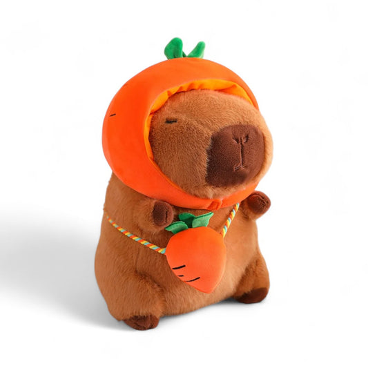 Peluche capybara marron avec un chapeau en forme de carotte et un petit sac assorti, sur fond blanc.