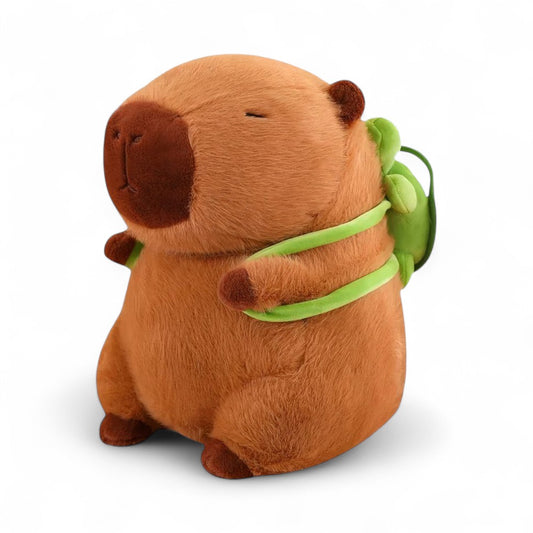 Peluche capybara marron avec sac à dos tortue verte, assis sur fond blanc.