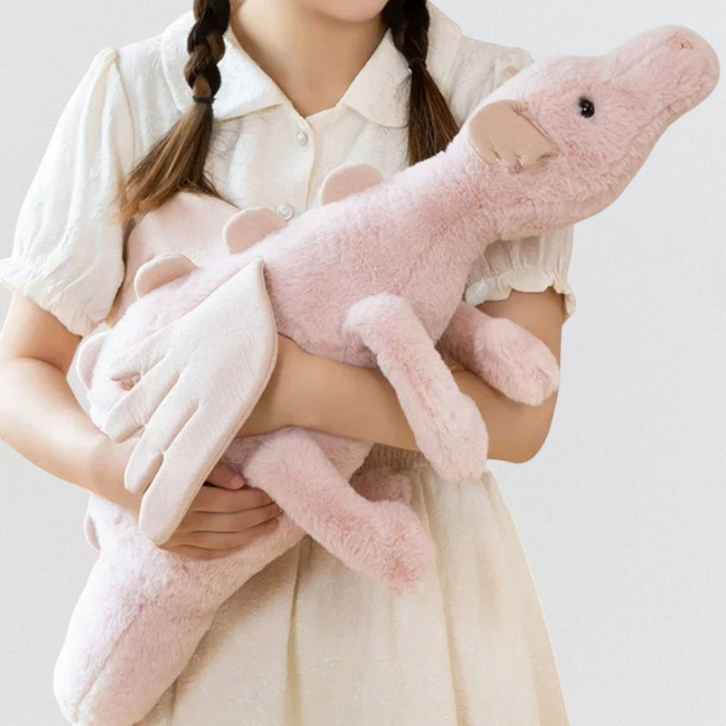 Dragon en peluche aux couleurs pastel - coloris rose tenu dans les bras d'une fillette