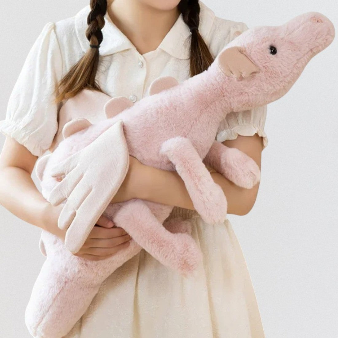 Dragon en peluche aux couleurs pastel - coloris rose tenu dans les bras d'une fillette