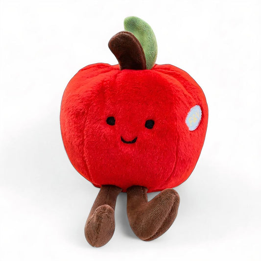 Peluche rouge en forme de pomme avec un sourire, des pattes marron et une petite tige verte sur la tête, posée sur fond blanc.