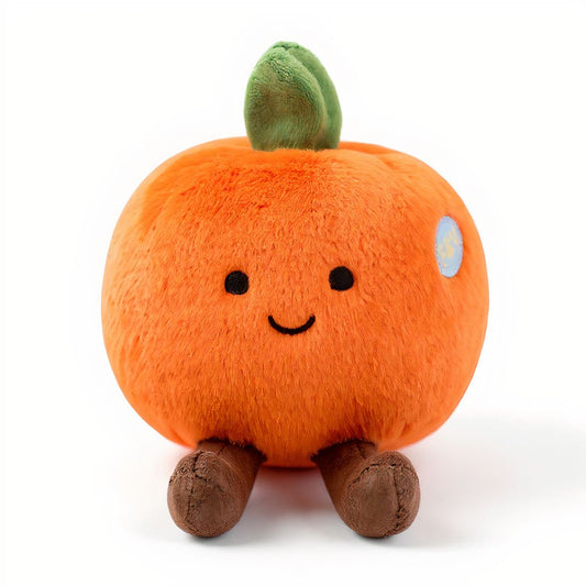 Peluche ronde en forme d’orange avec un petit sourire, des pattes marron et une feuille verte sur la tête, posée sur fond blanc.