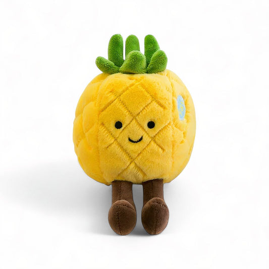 Peluche ananas jaune au visage souriant, pattes marron et feuilles vertes sur la tête, posée sur fond blanc.