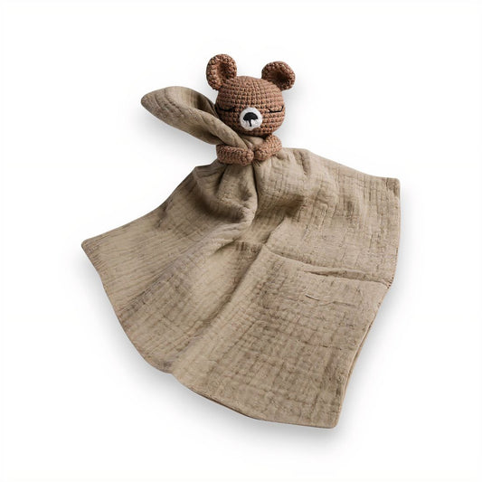 Doudou plat avec tête d’ourson crochetée tenant un lange en coton marron clair, sur fond blanc.