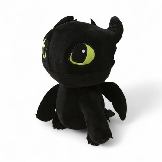 Peluche dragon noir, avec une grosse tête, et de grands yeux verts, sur fond blanc. 