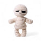 Peluche momie crème aux larges bandes et sourire brodé, sur fond blanc.