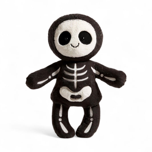 Peluche squelette noire et blanche au sourire doux, posée assise sur un plaid ou portée par un enfant.