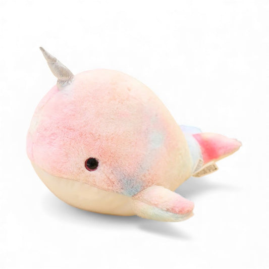 Peluche narval ronde et douce, aux couleurs pastel rose, bleu et jaune, avec une petite corne argentée sur la tête et deux nageoires de chaque côté, posée sur un fond blanc.