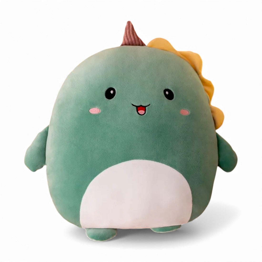 Peluche dinosaure verte toute ronde, avec petit ventre clair, yeux noirs ronds, pattes courtes et crêtes douces sur la tête et le dos, posée seule sur fond blanc.
