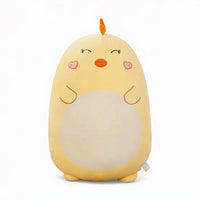 Grand coussin peluche poussin jaune, 45 cm, ventre crème, yeux fermés, joues en forme de cœur et petit bec orange, posé sur un canapé clair.