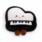 Peluche en forme de piano kawaii noir et blanc avec visage souriant et touches brodées, posée sur fond blanc.