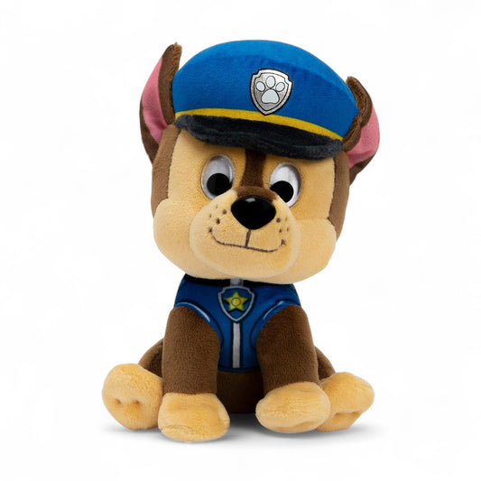 Peluche Chase marron et beige de la Pat’ Patrouille, en uniforme bleu, oreilles dressées, casquette bleue, assise sur fond blanc.