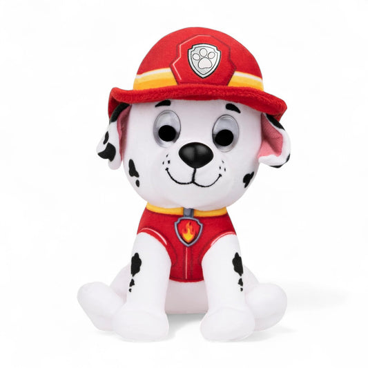 Peluche Marcus de la pat' patrouille, dalmatien blanc à taches noires, tenue rouge et casque de pompier rouge, assise et souriante sur fond blanc.