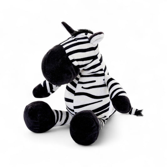 Peluche zèbre rayée noire et blanche, museau noir, grandes pattes et oreilles dressées,  assis sur fond blanc.
