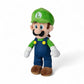 Peluche Luigi de Super Mario Bros, casquette verte avec “L”, salopette bleue, moustache noire, yeux bleus, en position debout sur fond blanc.