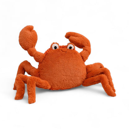 Peluche crabe orange, avec de grandes pinces, des yeux blancs sur le sommet et un sourire brodé ; sur fond blanc