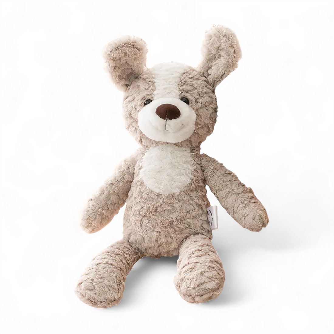 Chien en peluche beige et blanc, grandes oreilles souples, museau marron, assis sur fond blanc.