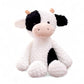 Vache en peluche blanche à taches noires, avec museau beige et cornes courtes, assise sur fond blanc.