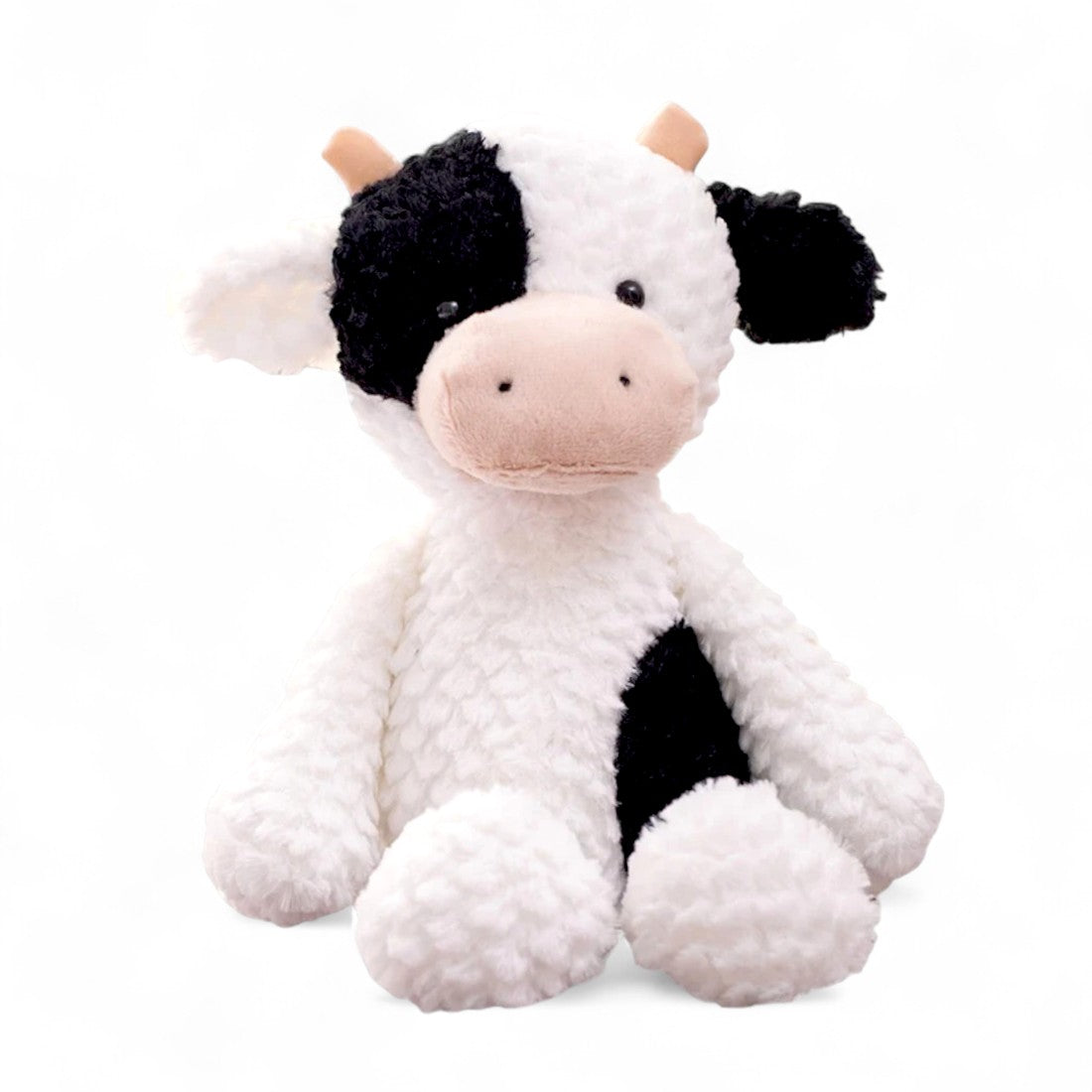 Vache en peluche blanche à taches noires, avec museau beige et cornes courtes, assise sur fond blanc.