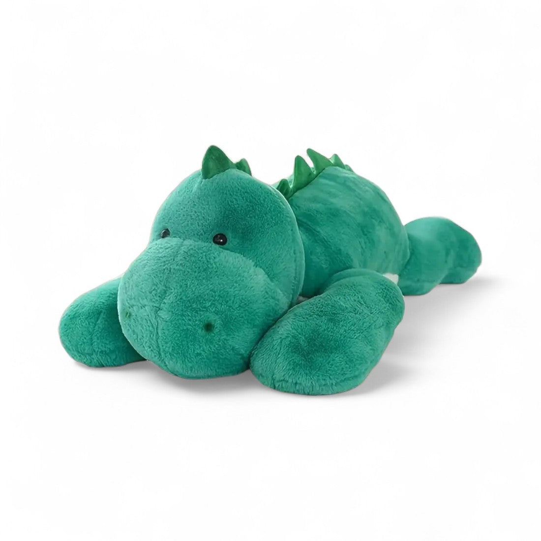 Dinosaure en peluche vert allongé, yeux brillants, crête sur le dos, posé sur fond blanc.