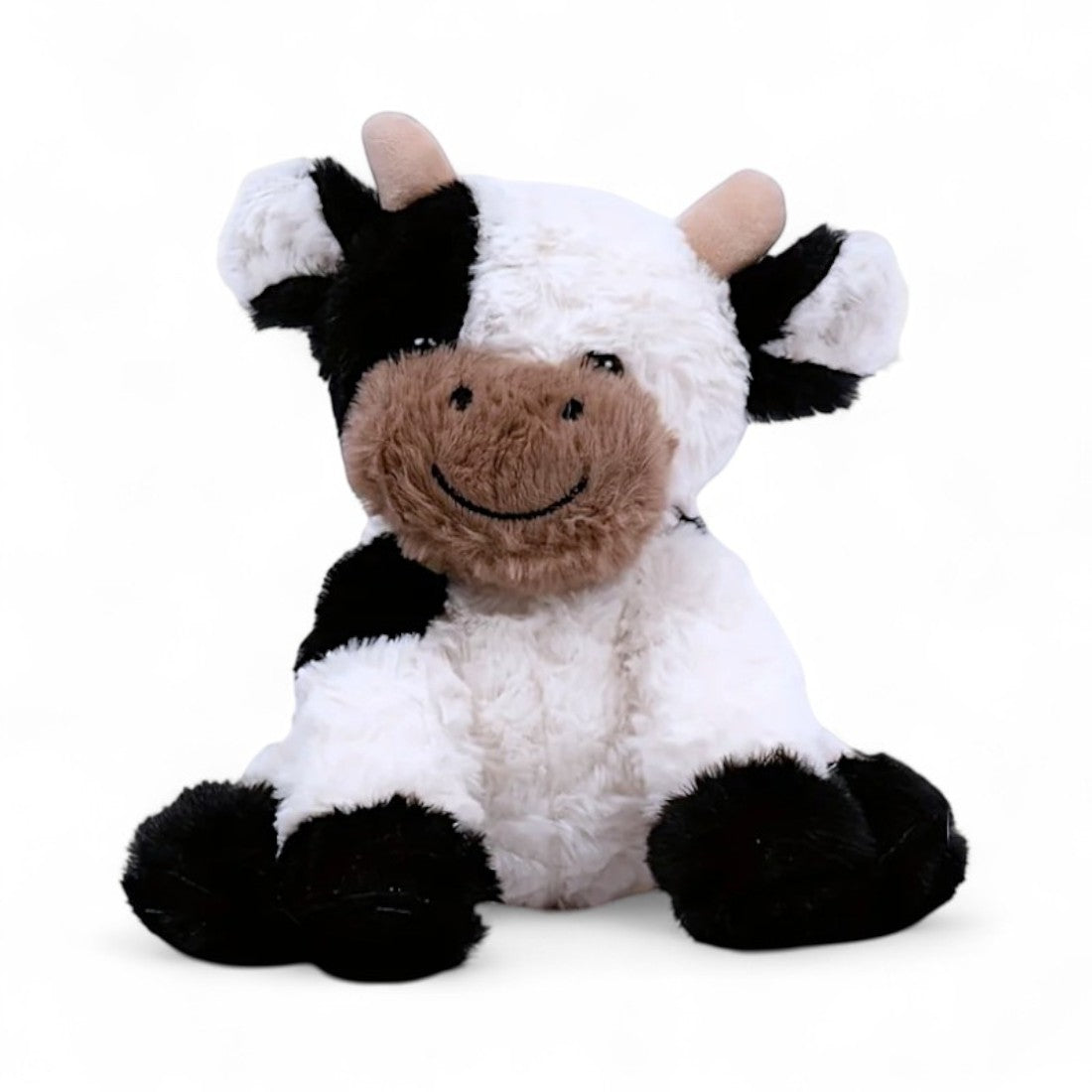 Vache en peluche blanche et noire, museau beige souriant, cornes courtes, oreilles rondes, assise sur fond blanc.