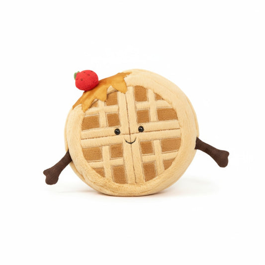 Peluche gaufre ronde beige, avec une fraise rouge sur la tête, deux petits bras marron et un visage souriant, posée sur fond blanc