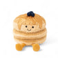 Peluche pancakes beige avec un visage souriant, jambes jaunes et petites myrtille bleues sur le dessus, assise sur fond blanc