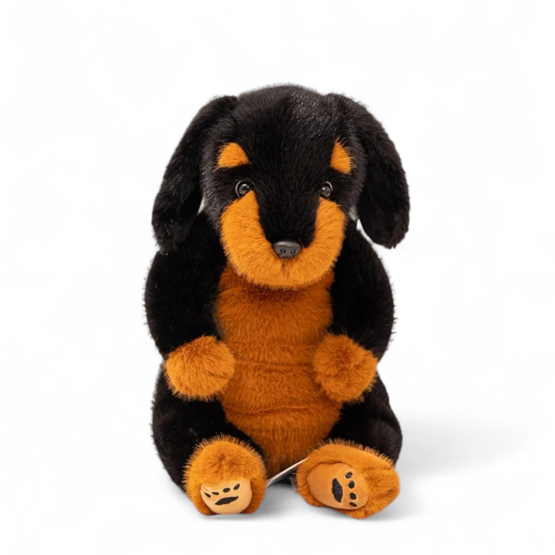 peluche rottweiler noir et orange assis, truffe noire, regard réaliste, sur fond blanc.