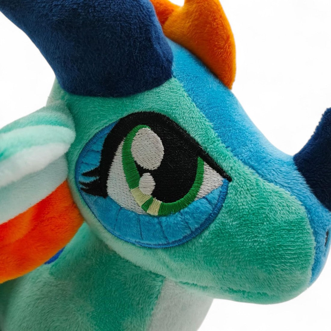 Peluche dragon féérique turquoise flamboyant - gros plan sur l'œil brodé