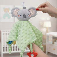 Doudou carré vert tête peluche koala avec anneau sensoriel - tenu par l'oreille dans une chambre d'enfant