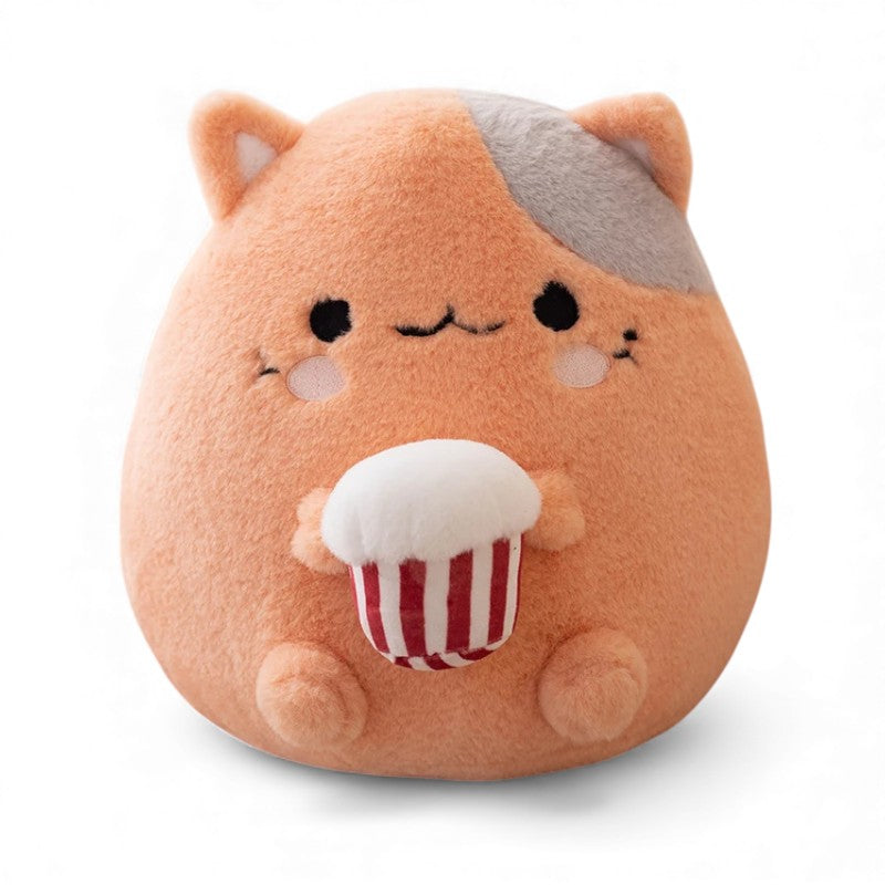 Coussin peluche rond représentant un chat orange avec une tache grise sur la tête, des joues roses, un nez rose, des petites oreilles rondes, tenant un cupcake rouge et blanc au ventre, posé sur fond blanc