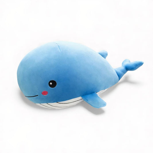 Peluche baleine bleue, allongée avec nageoires et queue souples, joues rose, posée sur un canapé ou sur fond blanc.