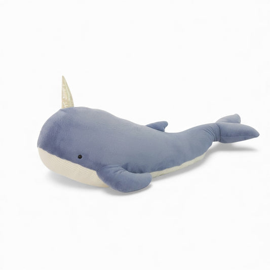 Peluche baleine couleur bleu, avec corne brillante sur le front, grande taille pour câlin, posée sur fauteuil, lit ou sol dans un intérieur lumineux.