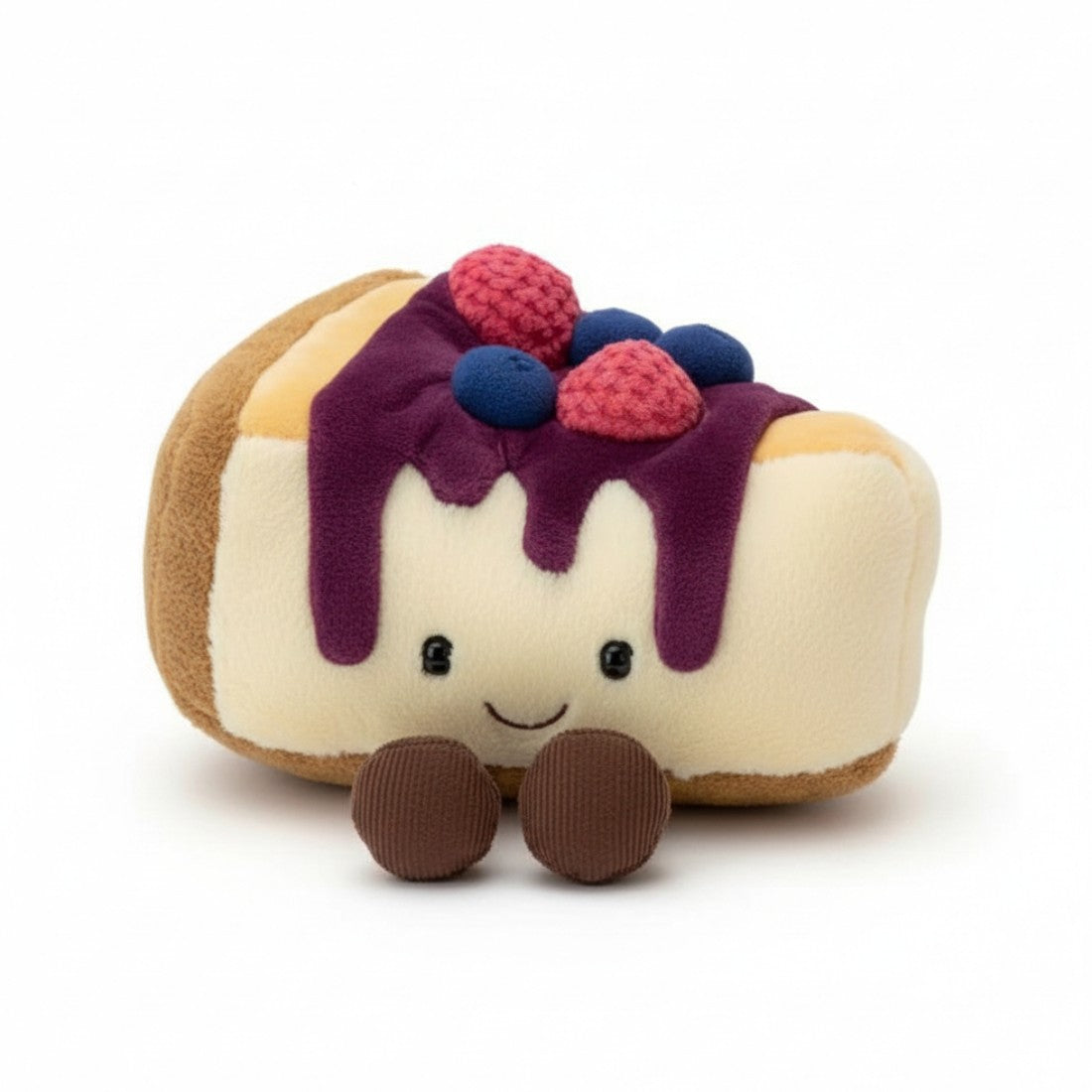 Peluche en forme de part de gâteau cheesecake beige crème avec coulis violet coulant, petites myrtilles bleues et framboises roses sur le dessus, visage souriant aux grands yeux ronds et bouche en arc, deux petites pattes marron en dessous, sur fond blanc.