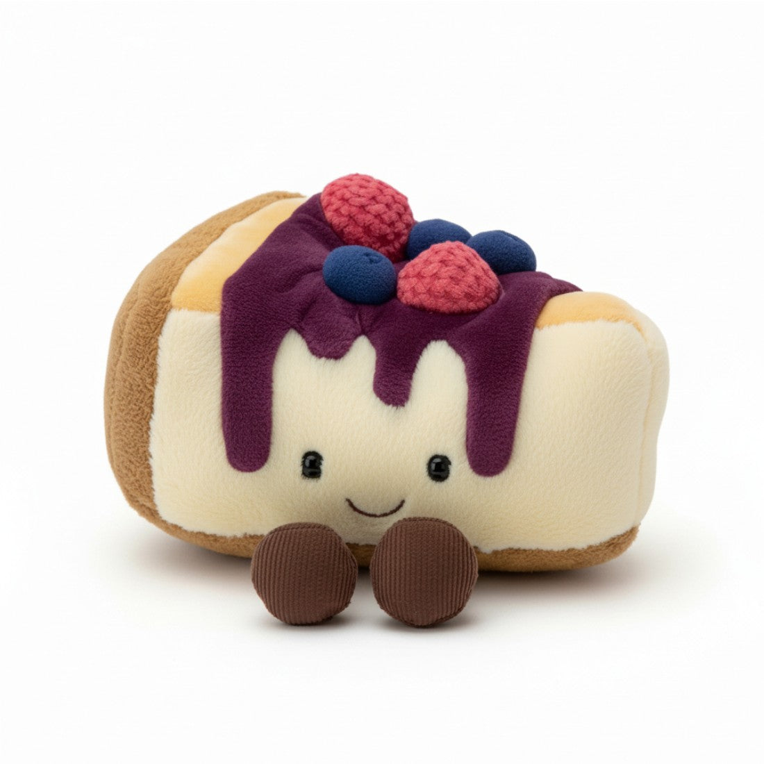Peluche en forme de part de gâteau cheesecake beige crème avec coulis violet coulant, petites myrtilles bleues et framboises roses sur le dessus, visage souriant aux grands yeux ronds et bouche en arc, deux petites pattes marron en dessous, sur fond blanc.