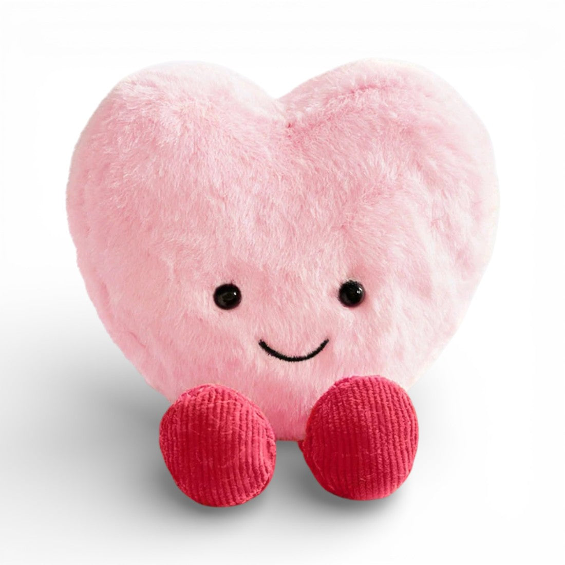 Une peluche en forme de cœur rose doux et duveteux, avec un grand sourire joyeux, deux yeux ronds noirs brillants et deux petites pattes en tissu tricoté rouge en bas, posée sur un fond blanc uni