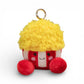 Peluche kawaii en forme de pop corn de 12 cm, base rouge et blanche rayée, pop corn jaune duveteux abondant sur le haut, grands yeux noirs brillants, joues roses, sourire joyeux, deux pattes rouges potelées en bas, anneau doré attaché sur le dessus, sur fond blanc.