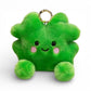 Peluche kawaii en forme de trèfle à quatre feuilles vert vif, grands yeux noirs brillants, joues roses rondes, sourire attendrissant, multiples feuilles duveteuses, deux petites pattes vertes potelées en bas, anneau doré sur le dessus, sur fond blanc.