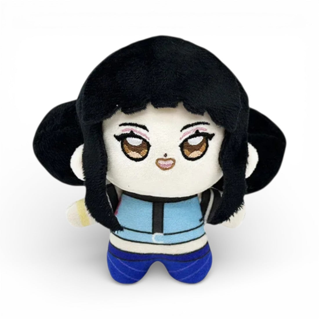 Peluche petite fille avec des cheveux noirs longs encadrant le visage, de grands yeux brillants brodés, habillée d'une tenue bleu foncé à motifs et pantalon bleu, sur fond blanc.