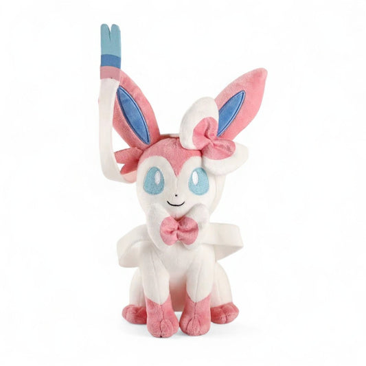Peluche Pokémon Nymphali rose et bleu assis avec grands rubans, yeux bleus et sourire tendre, sur fond blanc.